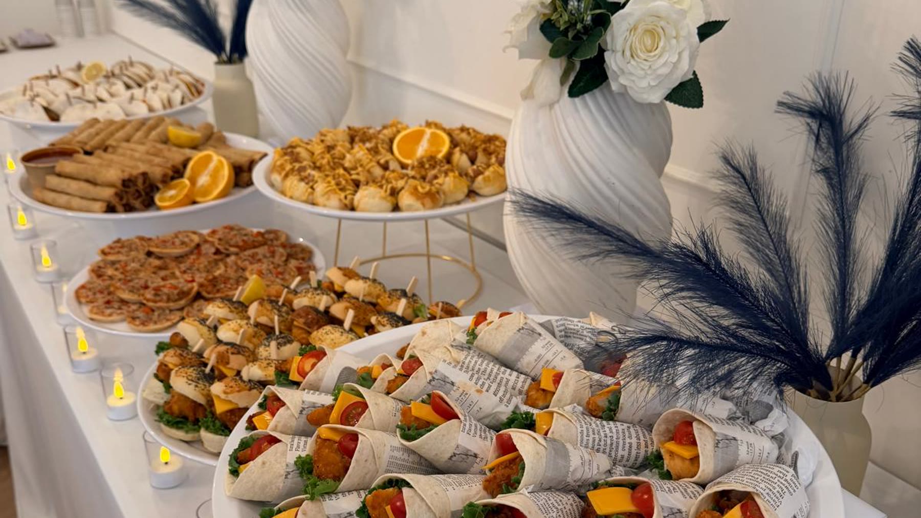 Gedekt buffet met witte rozen, donkere pampas en schalen vol wraps en hapjes