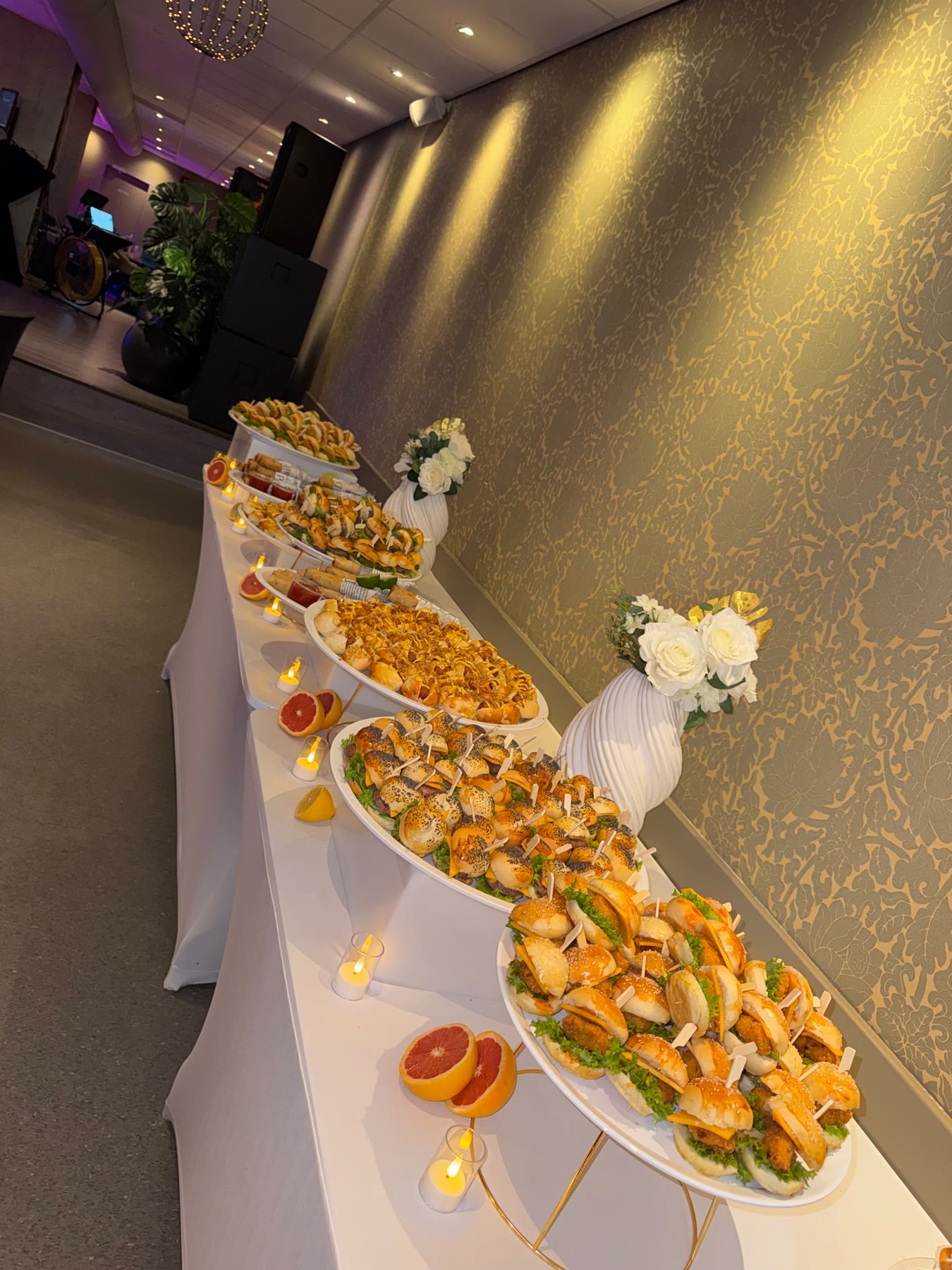 Lang gedekt buffet in warm licht, met schalen hapjes en bloemen