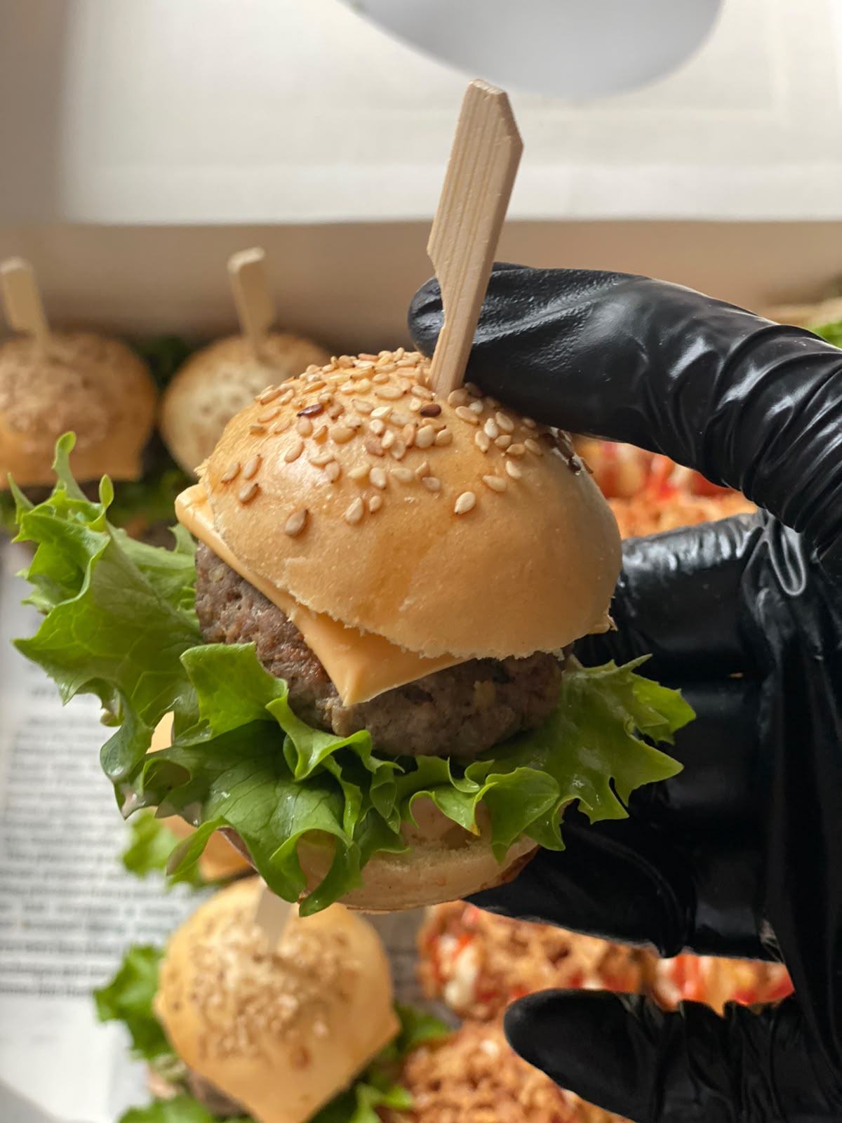 Mini hamburger met sesambol, vastgehouden boven een schaal