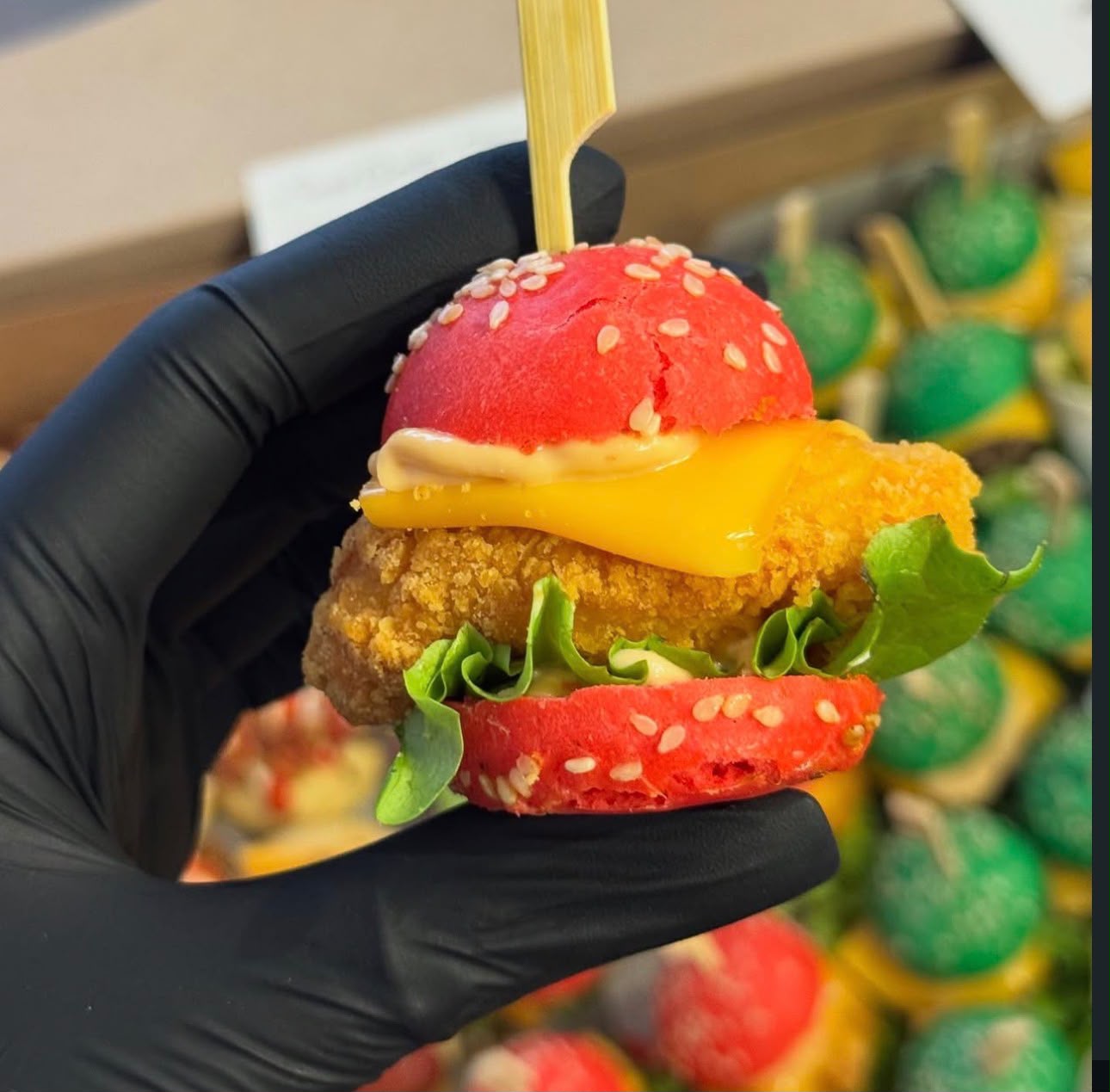 Mini kipburger met rood broodje en cheddar, in de hand